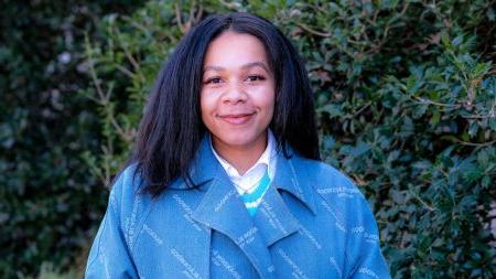 Jasmyne Yeldell standing in front of bushes with blue jacket on.